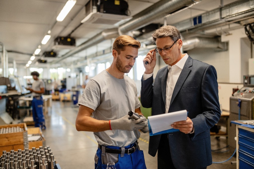 Engineer and plant manager reviewing production reports on a steel factory floor